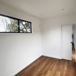 Finished interior room of a converted shipping container with wood flooring and large windows